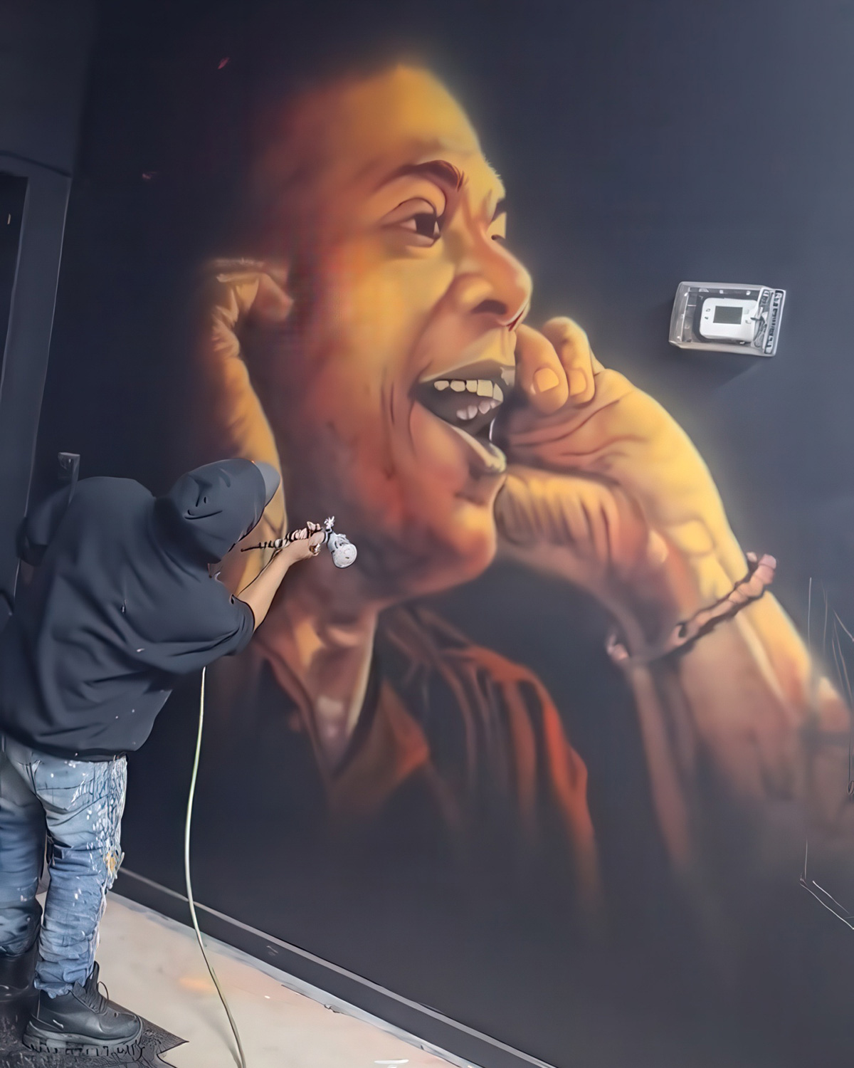 An artist airbrushing a large portrait mural at La Sombra Art Studio